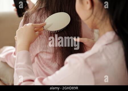 Close-up image of woman brushing and detangling long hair of her friend Stock Photo