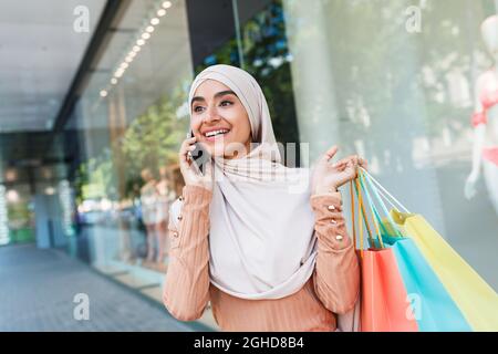 Happy cute young arab woman in hijab look ad about huge sale, enjoys modern shopping with a lot of packages Stock Photo
