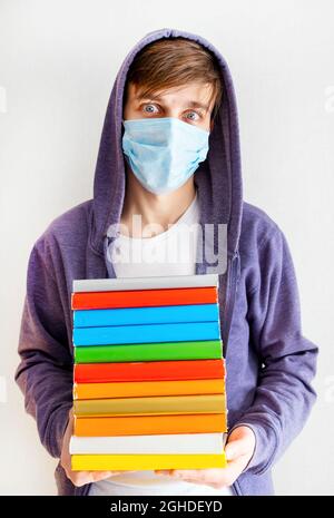 Surprised Young Man in a Flu Mask hold a Books by the White Wall in the Room Stock Photo