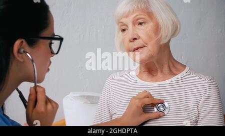 blurred nurse in eyeglasses examining aged woman with stethoscope Stock Photo
