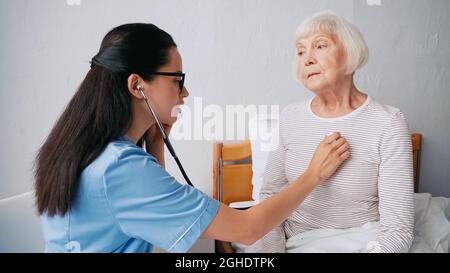 blurred nurse in eyeglasses examining senior woman in bed Stock Photo