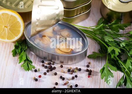 Canned seafood, whole shelled clams served on wooden table with parsley and pepper Stock Photo