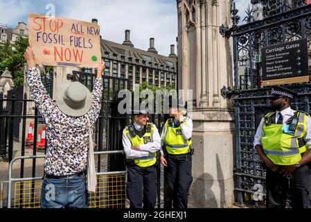 Extinction rebellion activist with placard Stop all new fossil fuels and police officers in front of the Houses of Parliament, Parliament Square, London, UK 06.09.2021 Stock Photo