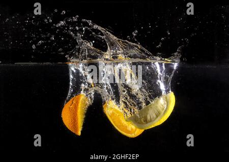 Closeup of delicious slices of lemons and oranges splashing in the water on a black background Stock Photo