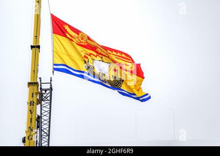 Saint John, NB, Canada - August 14, 2021: Large New Brunswick flag flying from an Irving crane. Foggy day with obscured harbor bridge behind. Stock Photo