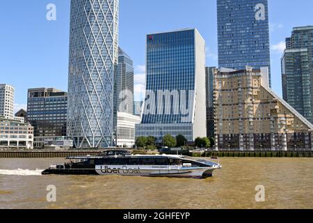 London, England - August 2021: Water taxi operated by Thames Clippers on the River Thames passing Canary Wharf. The service is sponsored by Uber Stock Photo