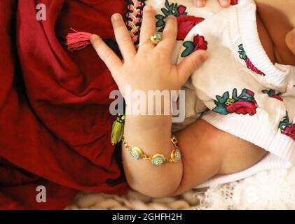 baby girl arm closeup with bracelet ring in tiny finger colorful floral dress Stock Photo