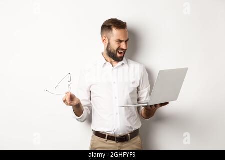 Confused manager looking at laptop, standing disappointed against white background Stock Photo