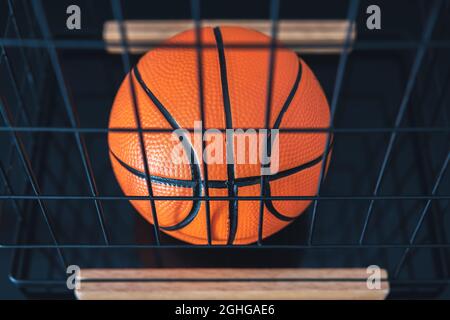 New, orange basketball ball located in a metal basket on a dark surface. Stock Photo