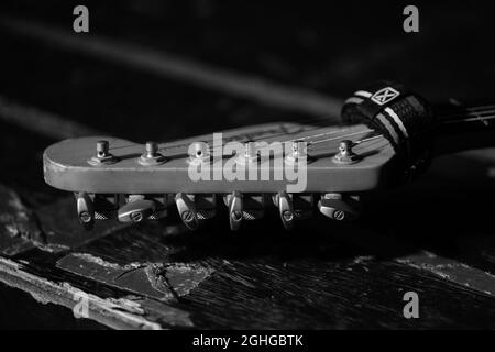 Greyscale closeup view of the headstock of the guitar on a wooden surface Stock Photo