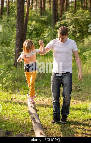 Caucasian girl of 6 years old walking on a log holding dad's hand. Father and daughter playing together,laughing and having fun. Happy Family activity Stock Photo