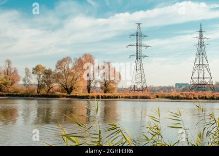 High-voltage power lines crossing the river. High voltage power transmission towers on the background of an autumn landscape. Stock Photo