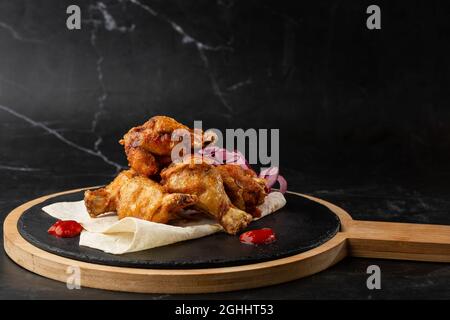 baked buffalo chicken wings with sesame seeds, onion and chili slices on black wooden Stock Photo