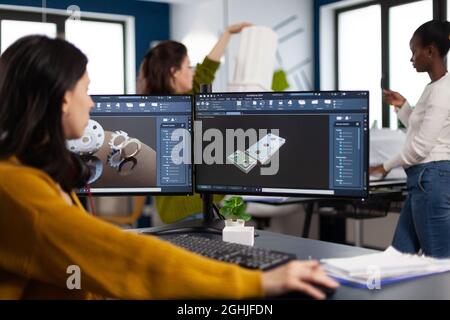 Industrial engineer woman working at pc with two monitors, screens showing CAD software with 3D architecture prototype of gears mechanical piece. Entrepreneur working in creative construction office Stock Photo