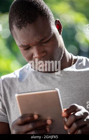 Portrait of young attractive Afro American man using tablet in park, modern technology. Stock Photo