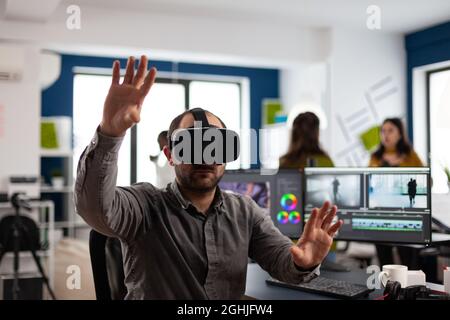 Video editor experiencing virtual reality headset, gesturing, editing film montage using post production software working in creative company office. Videographer using VR headset in multimedia agency Stock Photo
