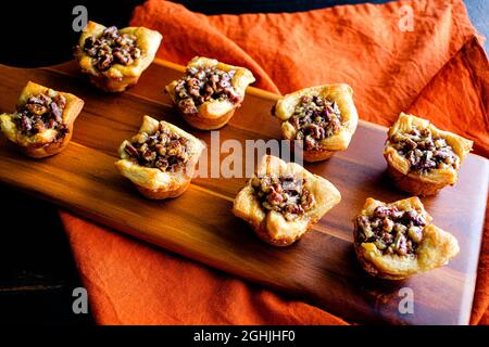 Pecan Pie Tartelettes Served on a Wooden Cutting Board: Individual pecan pie tarts displayed on a wood cutting board Stock Photo
