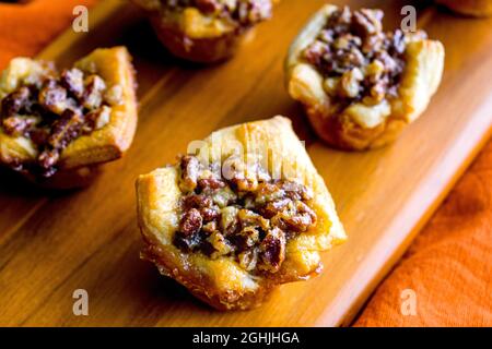Pecan Pie Tartelettes Served on a Wooden Cutting Board: Individual pecan pie tarts displayed on a wood cutting board Stock Photo