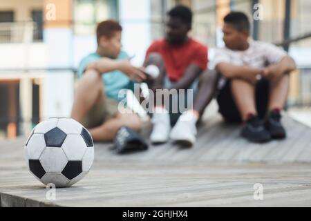 Focus on soccer ball on wooden podium outdoors, black father talking to sons in background Stock Photo