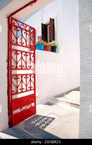 A red gate and flower pots on a wall in the traditional village of Megalochori in Santorini, Greece. Stock Photo