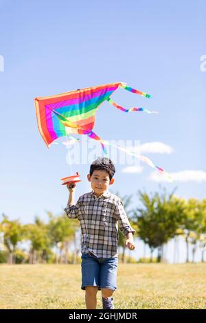 Happy boy running with kite on meadow Stock Photo
