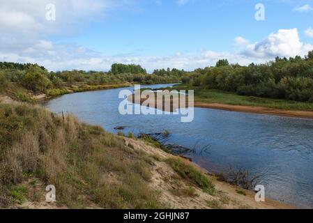 A picturesque river bank in early autumn with grass on the bank changing its color from green to yellow. Stock Photo