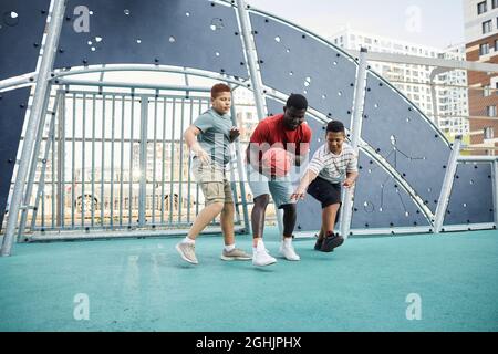 African-American father holding basketball while fighting for it while playing with sons on sports ground Stock Photo