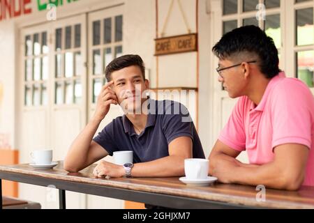 Two young men relax drinking coffee and talking in an urban latin locale. Stock Photo