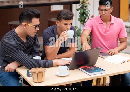 Three young entrepreneurs have coffee in the open air while doing their jobs. Stock Photo