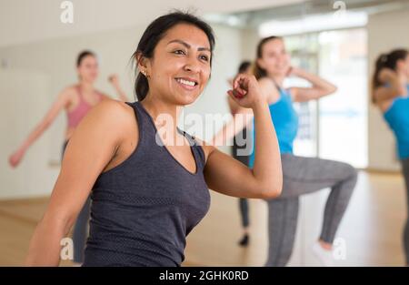 Cheerful hispanic woman practicing vigorous lindy hop movements in group dance class. Stock Photo