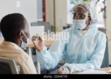 Medical nurse in protective suit and face shield telling patient to be ready for nasal swab for coronavirus testing Stock Photo