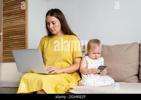 Unplugging mother after work. Child using mobile phone while mom working remotly at home Stock Photo