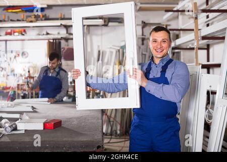 Production workers in coverall with different finished PVC profiles and windows at factory Stock Photo