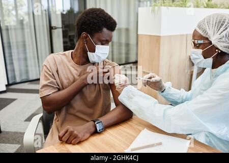 Young African American man sitting at doctors office and getting flu shot in his arm Stock Photo