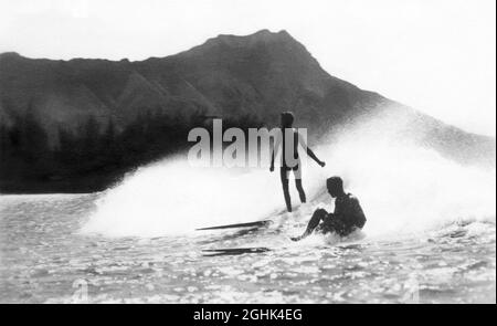 Early 20th century vintage surfing photo of surfers riding a wave on wooden longboards in Waikiki, Honolulu, Territory of Hawaii, with Diamond Head in the background. (Photo by Roscoe Perkins, c1916.) Stock Photo