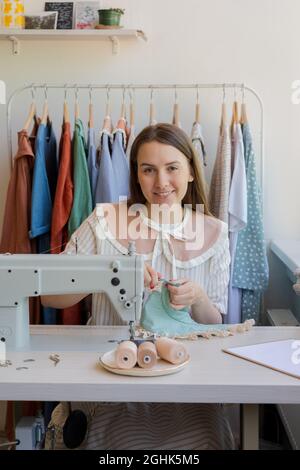 Smiling young woman sewing clothes at her own atelier or workshop Stock Photo