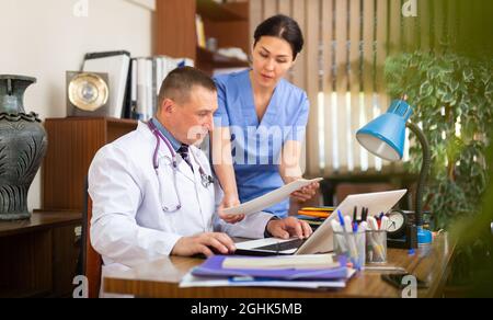 Two focused physicians working with case histories on laptop Stock Photo