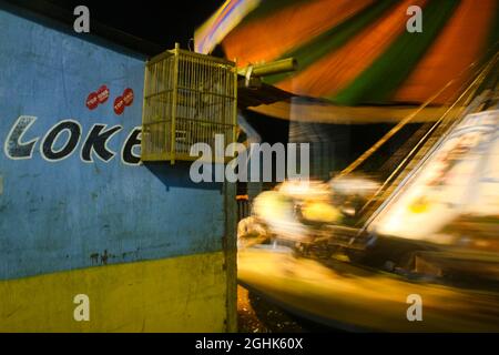 At the ticket booth for selling carousel games at a night market, bird cages are seen hanging on the counter board. Stock Photo