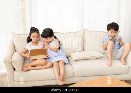 Cute children using digital devices on sofa Stock Photo
