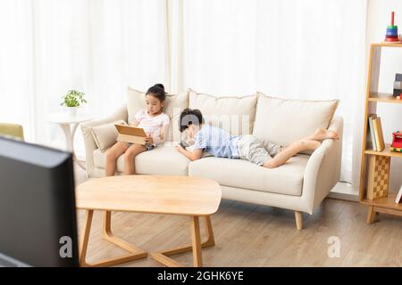 Cute children using digital devices on sofa Stock Photo