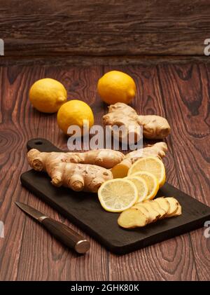 Ginger root, slices of ginger root and slices of lemon on a burned wood cutting board over brown wood background Stock Photo