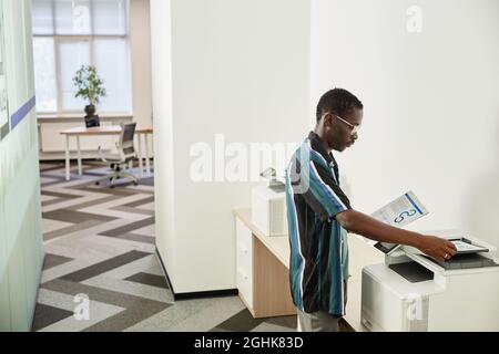 Serious Black office worker making copies of business charts and reports in photocopier Stock Photo