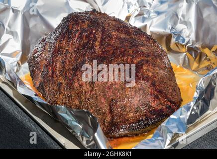 Portion of foil wrapped spicy seasoned roast beef brisket with juices opened to display the meat in an oven tray in close up Stock Photo