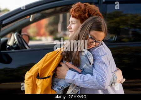 Mother and daughter standing in embrace against car outdoors in the morning Stock Photo