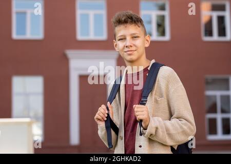 Contemporary youngster with backpack standing against building exterior and looking at you Stock Photo