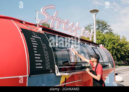 Young businessman in uniform and gloves wiping dust on windows of food track before working day Stock Photo