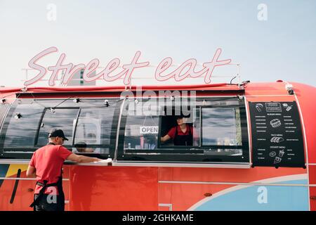Two young workers in uniform cleaning red food truck in the beginning of working day Stock Photo