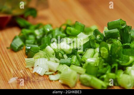 Cook cuts the recipe green onions on wooden board in the kitchen. Stock Photo