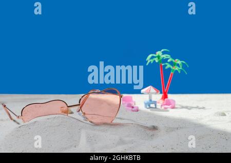 Sunglasses in the sand. Background is empty for advertising, demonstration of cosmetic products, items. Sea beach with sand on a blue background. Mock Stock Photo