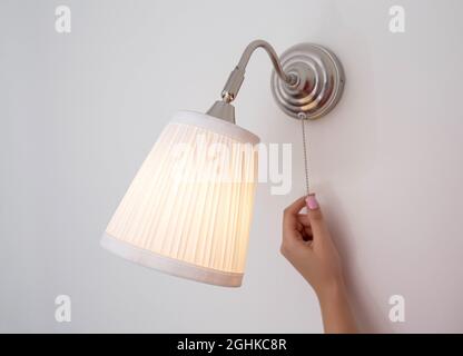 A woman's hand turns the wall sconce on and off with a rope. Night light above the bed Stock Photo